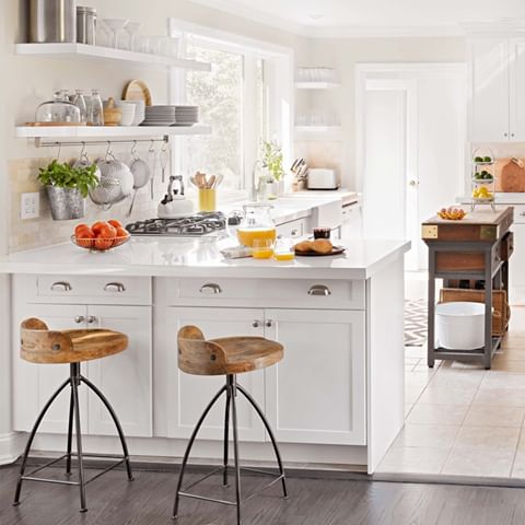 This primarily white kitchen could have easily taken a cold turn. But a few organic additions help the space feel warm and welcoming. Stone floors and backsplashes combine with wood-seat stools and a primitive island to boost interest without disturbing the room's bright spirit.✨ Tap the link in our bio for more white kitchen ideas we love. 📷: @annieschlechter | Producer: Melissa Feldman | Homeowner: Analisse Taft